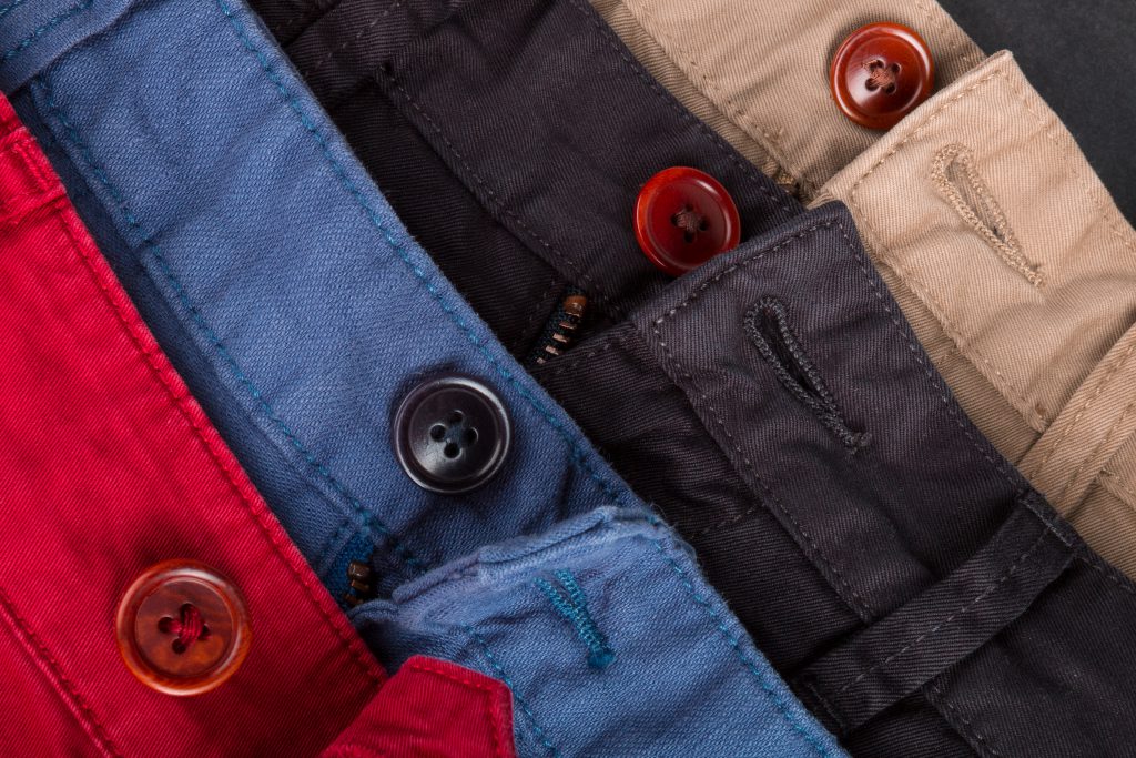 Fragment of four cotton twill pants red, blue, black, beige with open buttons. Close up.