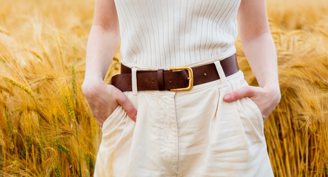 View on torso of woman in pants and belt with golden wheat on background